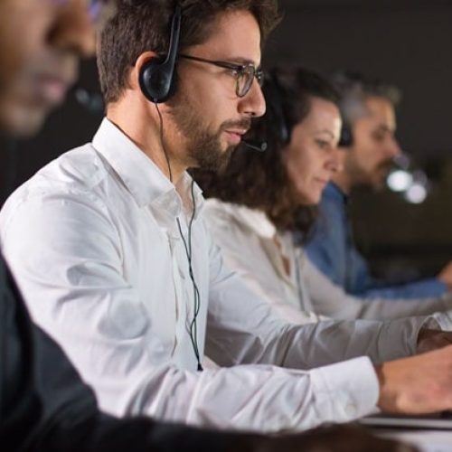 Side view of confident call center operator talking with client. Caucasian young man in eyeglasses typing on laptop while serving client. Call center concept